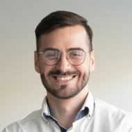 Portrait d'un homme souriant portant des lunettes et une chemise blanche.