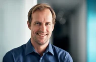Portrait d'un homme souriant portant une chemise bleue.