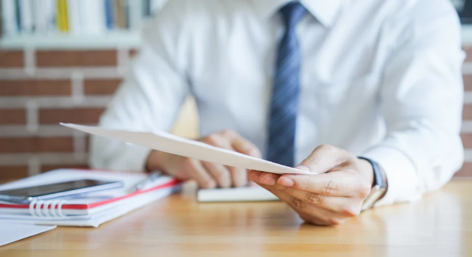 Personne en tenue professionnelle tendant un document au-dessus d'un bureau.