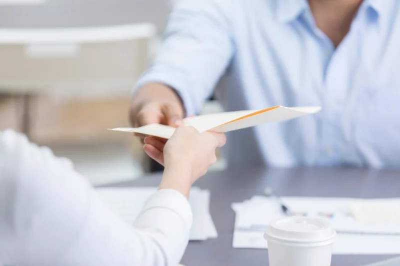 Personne remettant un document à une autre personne au-dessus d'un bureau.